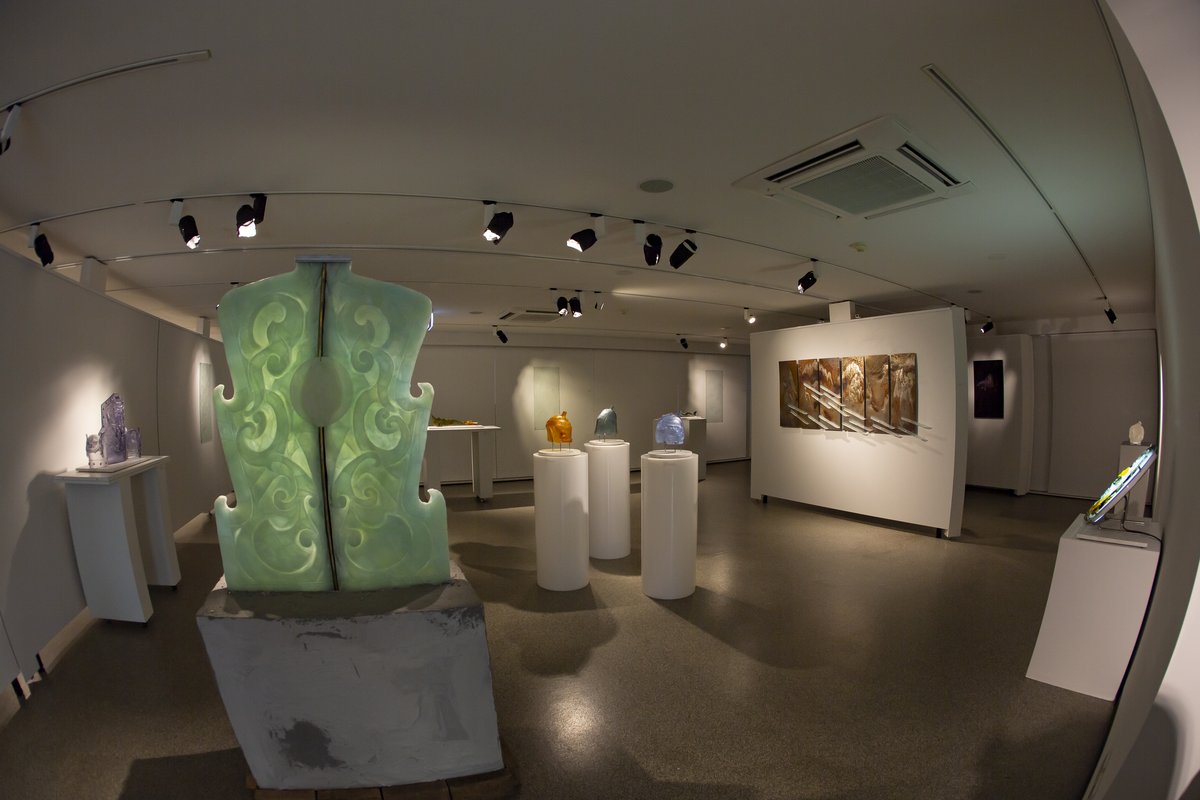 Fisheye photo of an exhibition featuring a painting series and various glass sculptures of armour.