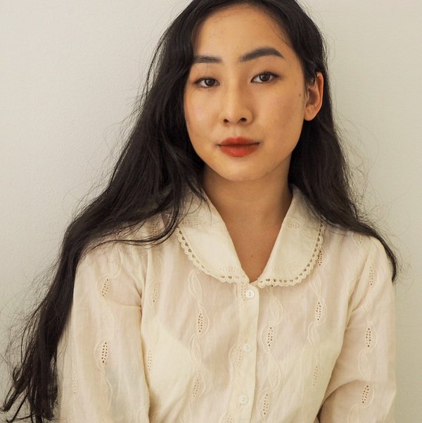 ​Head and shoulders portrait of Donnalyn Xu. She is wearing a long sleeve cream top, is sitting in front of a white background and have long dark hair.